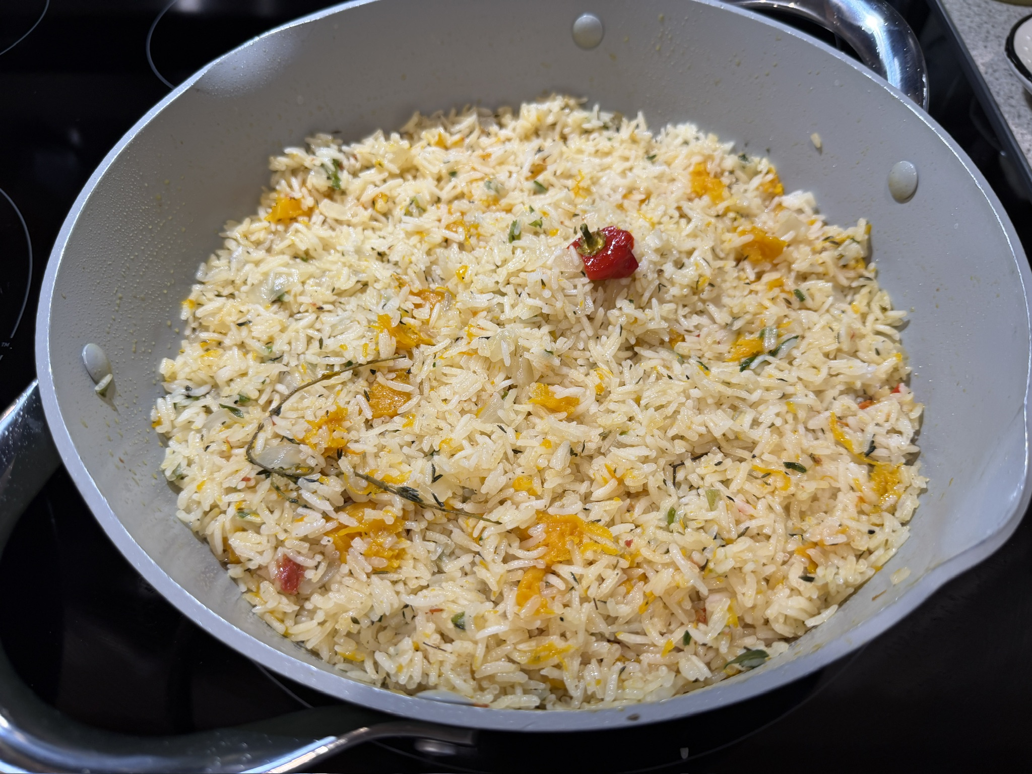 Jamaican pumpkin rice cooking in a pan with herbs and pumpkin