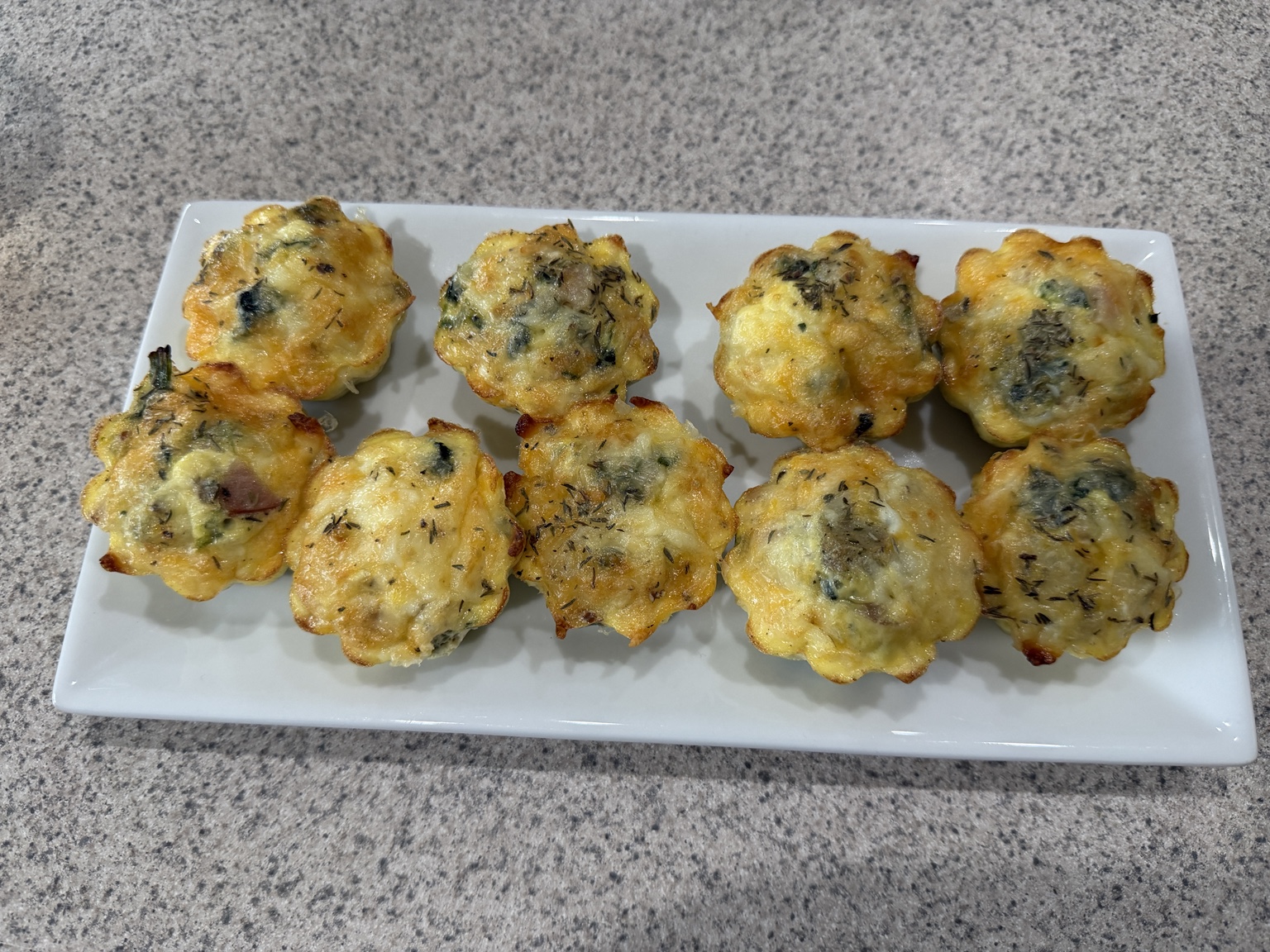 Golden egg bites with vegetables, ham, sausage, cheese, and herbs on a serving platter